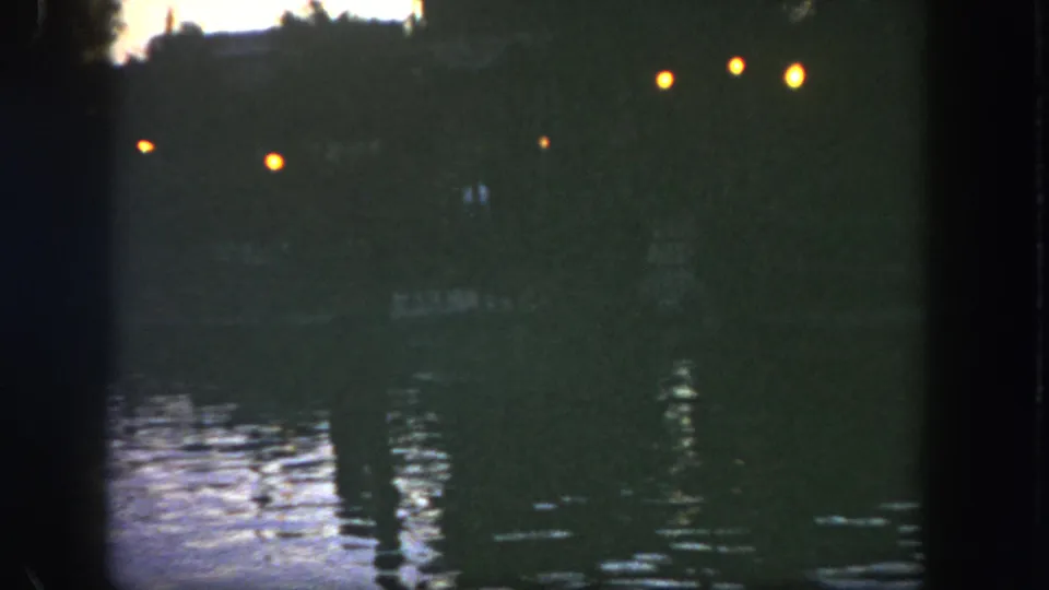 1962 Disneyland 8mm closing frame of a shadowed lakeside view with bright lamps and vertical reflections on the water.