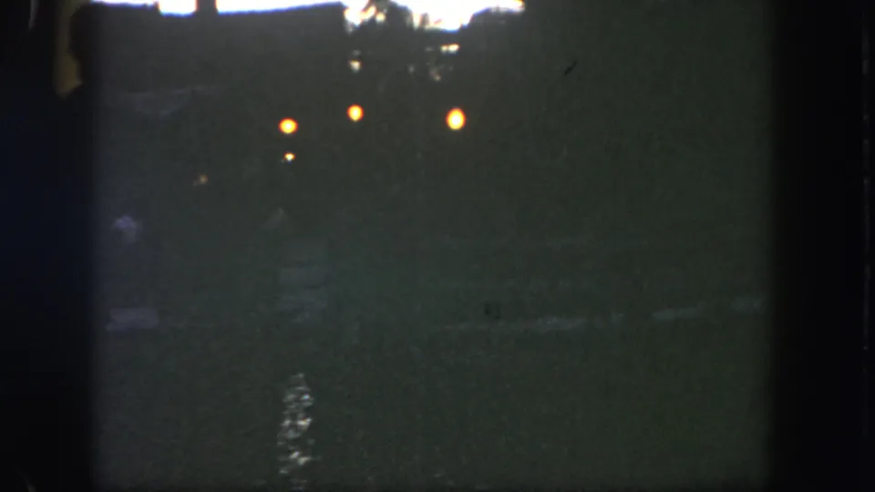 Low-light 1962 Disneyland home-movie frame showing faint waterfront lights and reflections across a dark river.