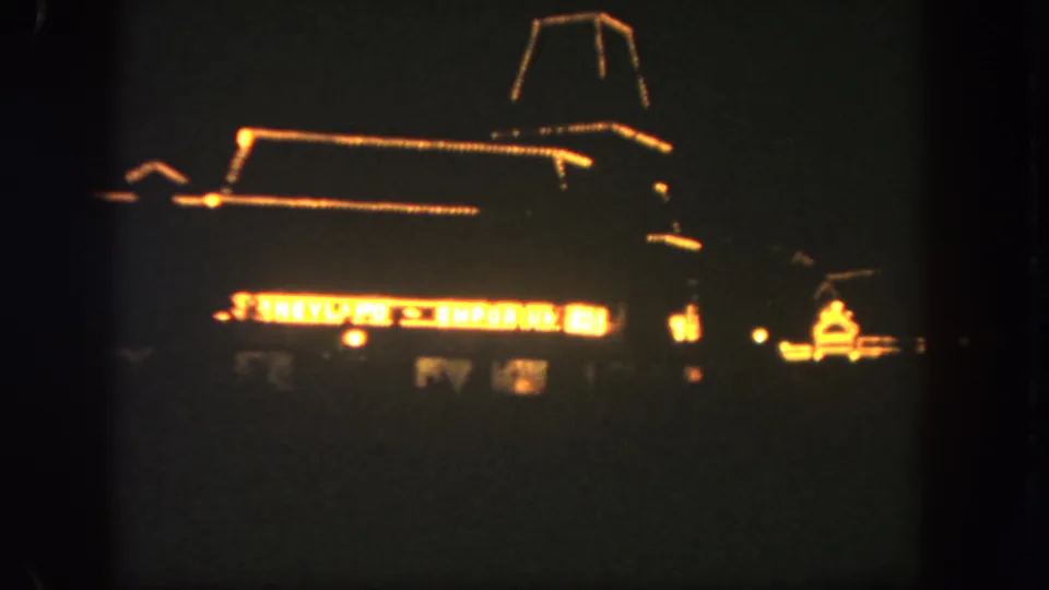 1962 Disneyland frame showing a bright restaurant or attraction sign, low roofline, and dark surrounding waterfront.