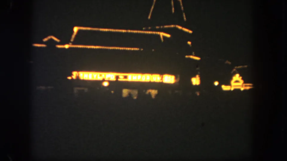 1962 Disneyland night frame with the Emporium exterior mostly silhouetted and defined by warm decorative lighting.