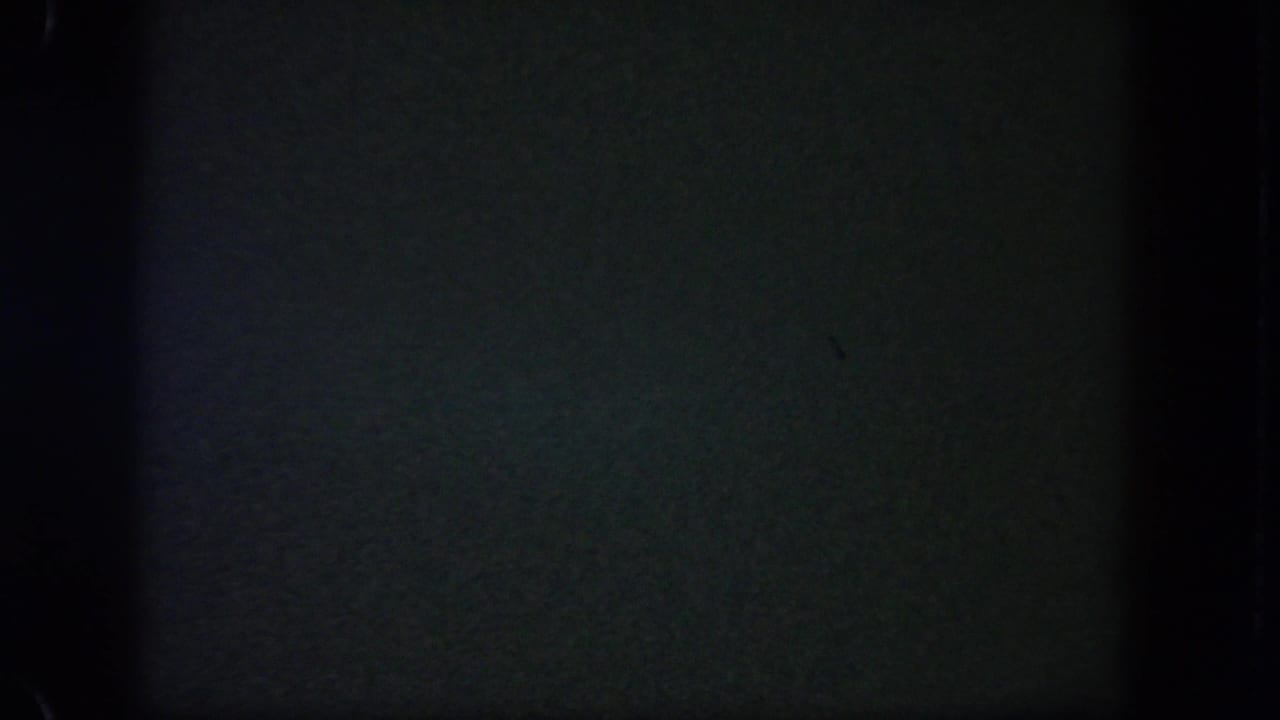 Underexposed 8mm frame from the Disneyland night clip, with little visible beyond dark film texture and edge shadows.