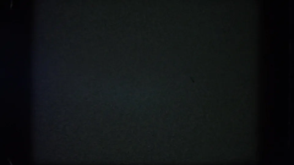 Underexposed 8mm frame from the Disneyland night clip, with little visible beyond dark film texture and edge shadows.