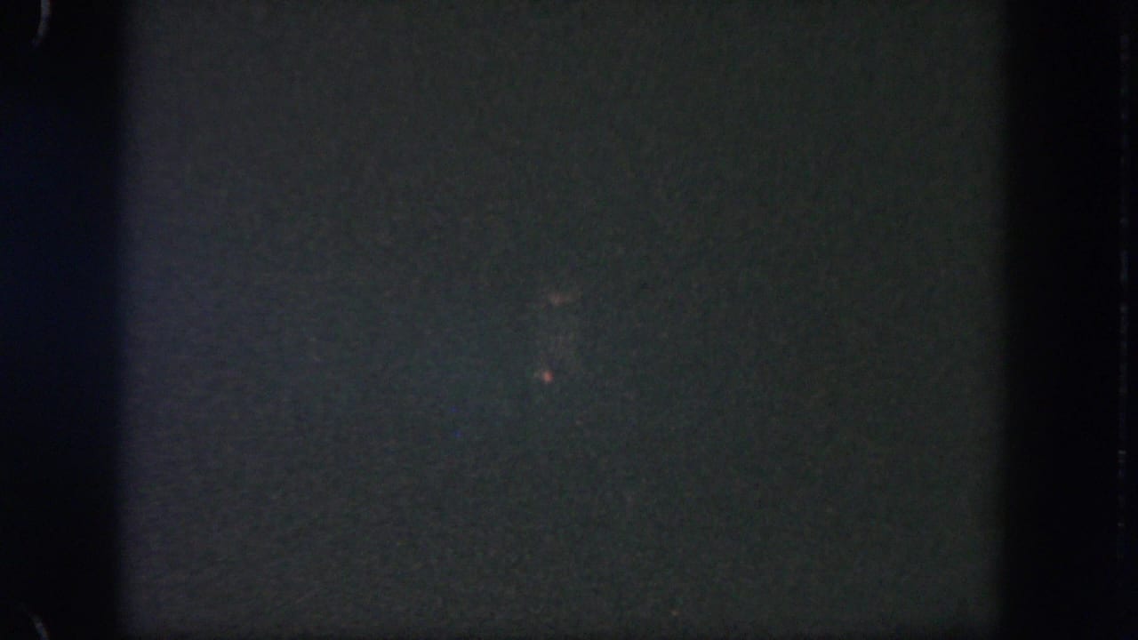 Very dark 8mm frame with grain, frame edges, and faint distant specks of light.