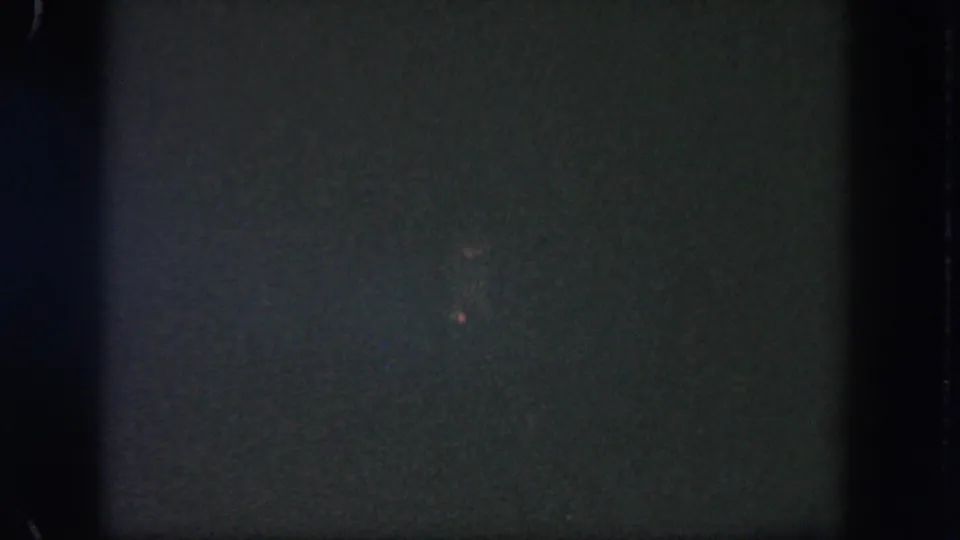 Dark 1962 Disneyland 8mm frame with heavy grain, visible film edges, and only faint points of light in the background.