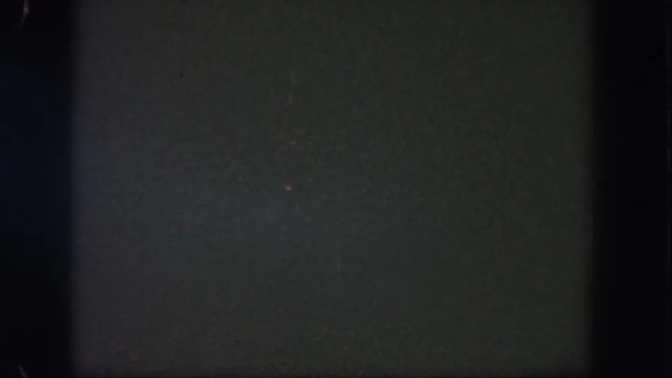 Mostly black 1962 Disneyland 8mm frame with heavy grain, dark borders, and only a few faint visible light points.