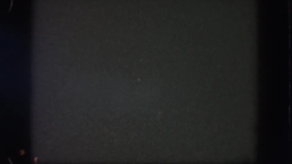 Underexposed 1962 Disneyland 8mm frame with dim distant lights, grain, and a soft vertical band at the left edge.
