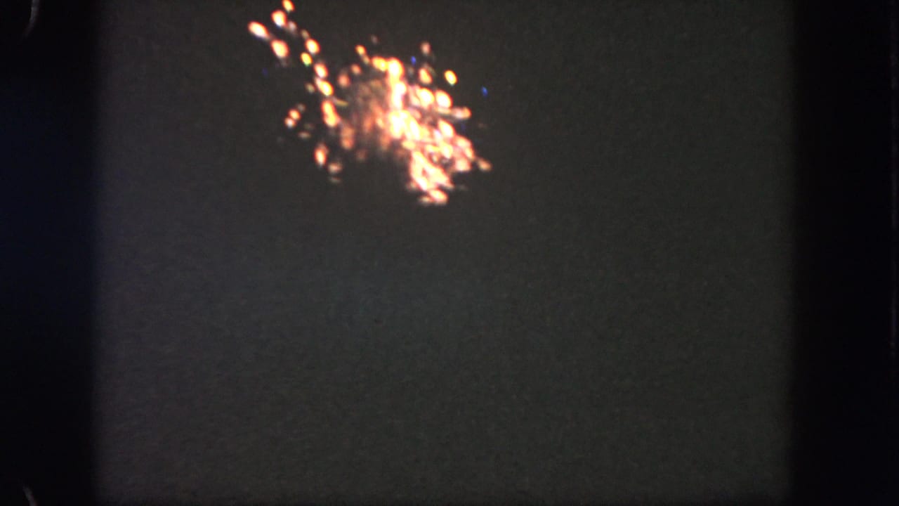 A small orange-white fireworks burst appears high in the dark sky in 1962 Disneyland 8mm footage.
