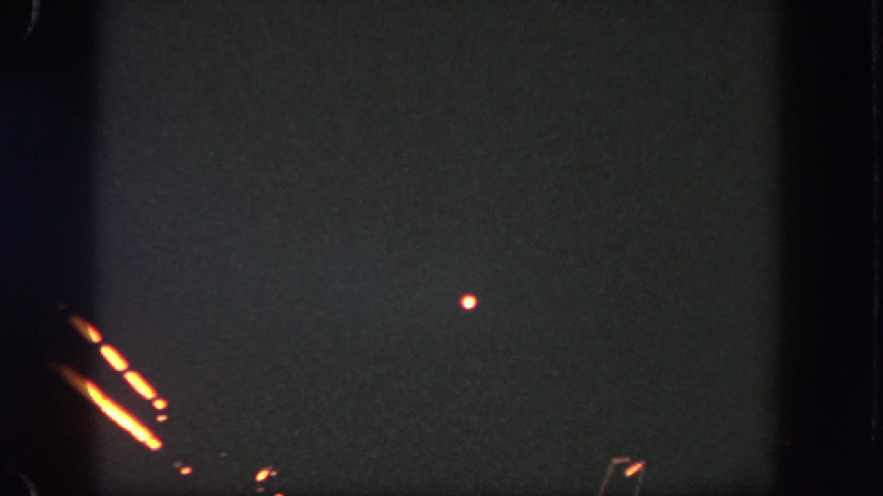 A dark Disneyland home-movie frame shows orange firework-like streaks and a small glowing point against grainy night exposure.