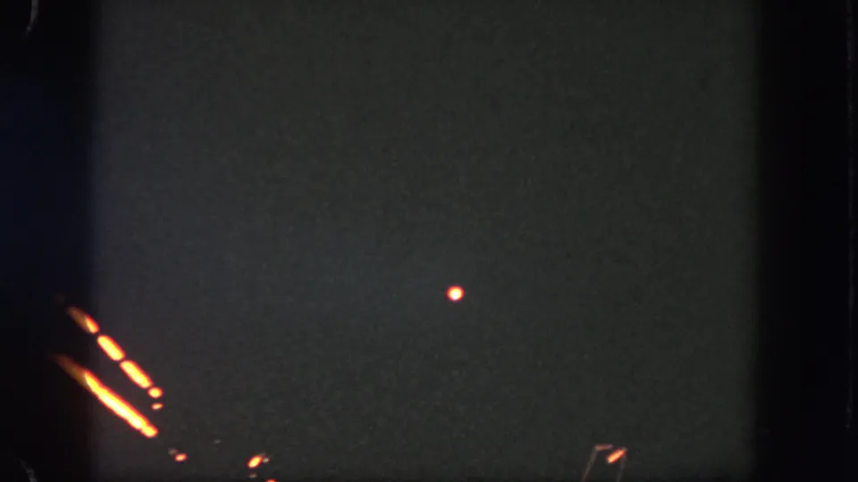 A dark Disneyland home-movie frame shows orange firework-like streaks and a small glowing point against grainy night exposure.