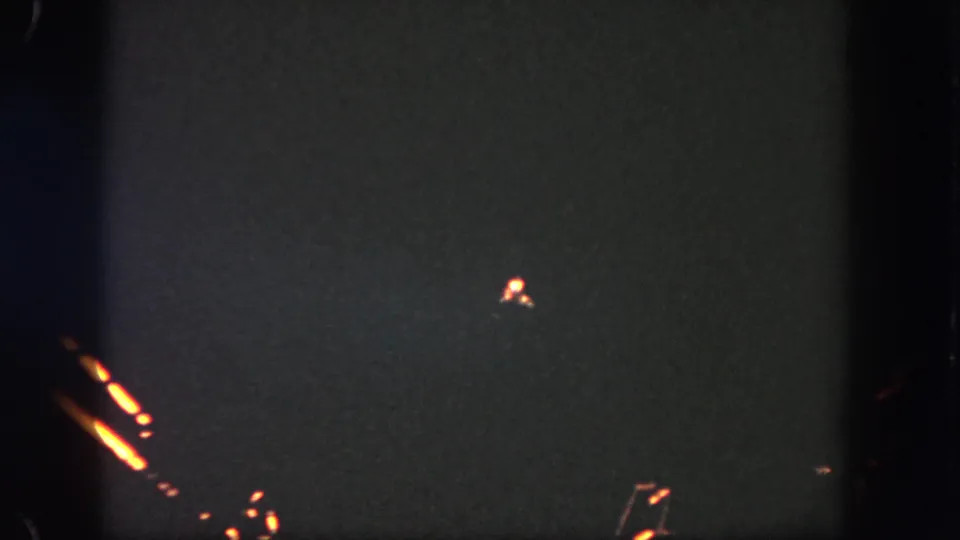 A grainy Disneyland night frame shows orange firework-like streaks, a few small sparks, and visible 8mm frame boundaries.