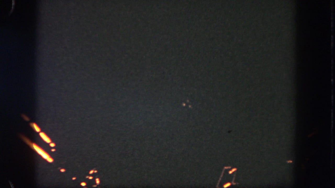 1962 Disneyland home-movie frame showing a dark night sky with orange firework trails and small glowing fragments.