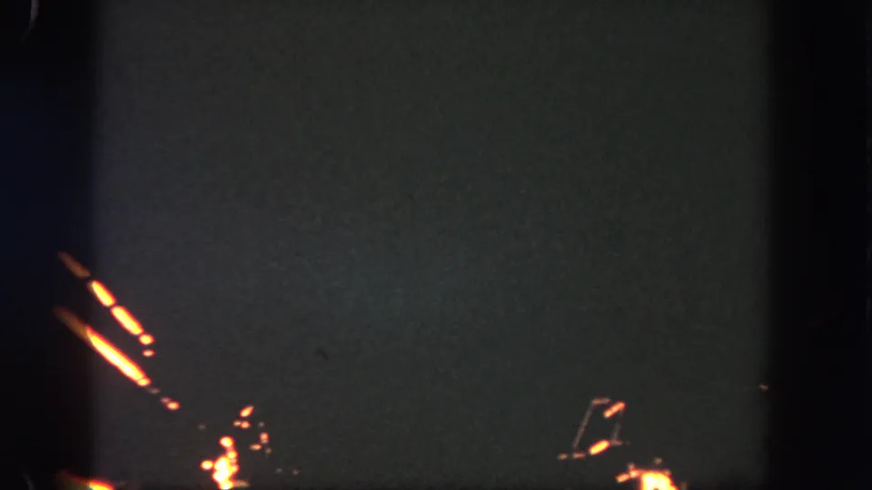1962 Disneyland home-movie frame showing orange firework trails near the lower left of a dark sky.