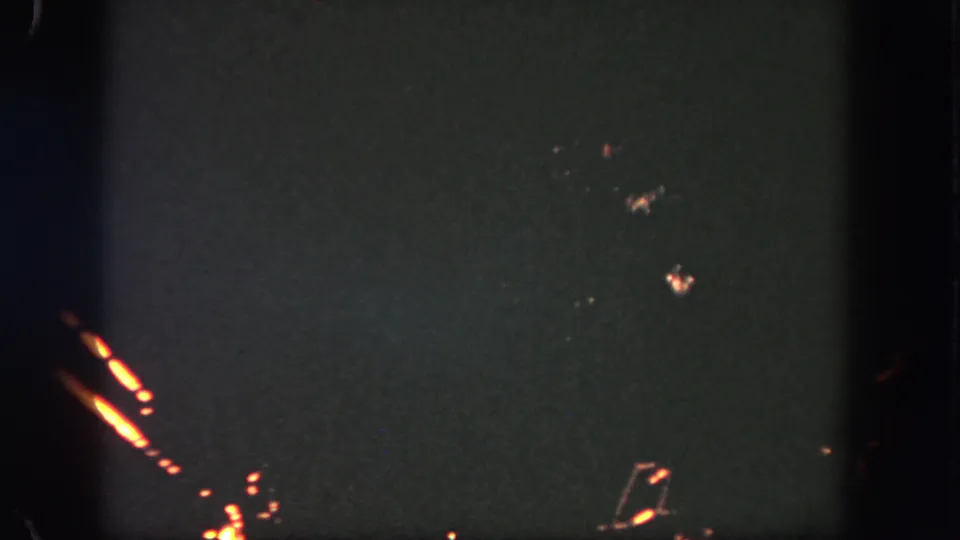 1962 Disneyland 8mm frame with edge firework trails and faint sparks spread across the dark sky.