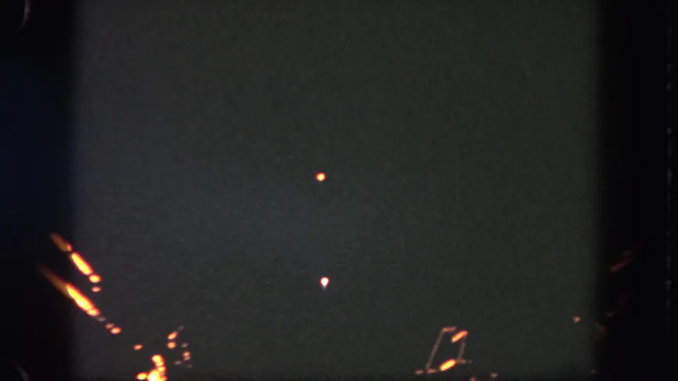 1962 Disneyland home-movie frame showing a dark night sky with orange light streaks and small bright points.