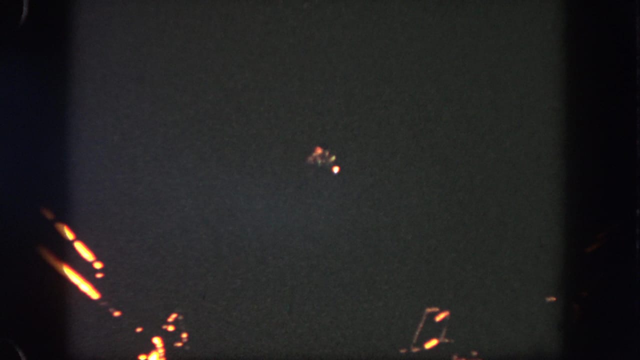1962 Disneyland nighttime frame with distant orange illumination and faint spark-like lights against the dark sky.