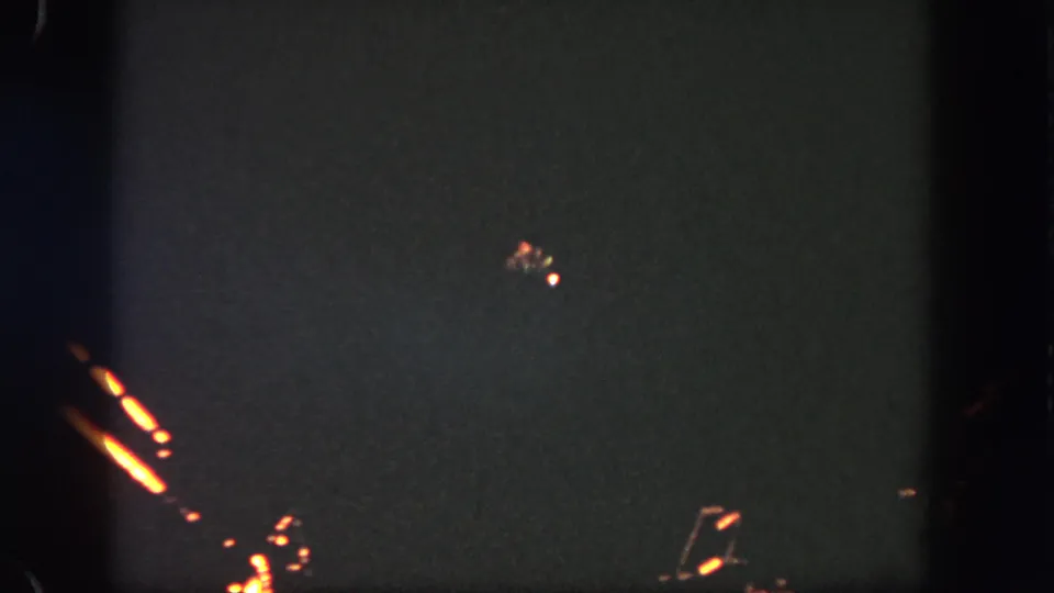 1962 Disneyland nighttime frame with distant orange illumination and faint spark-like lights against the dark sky.