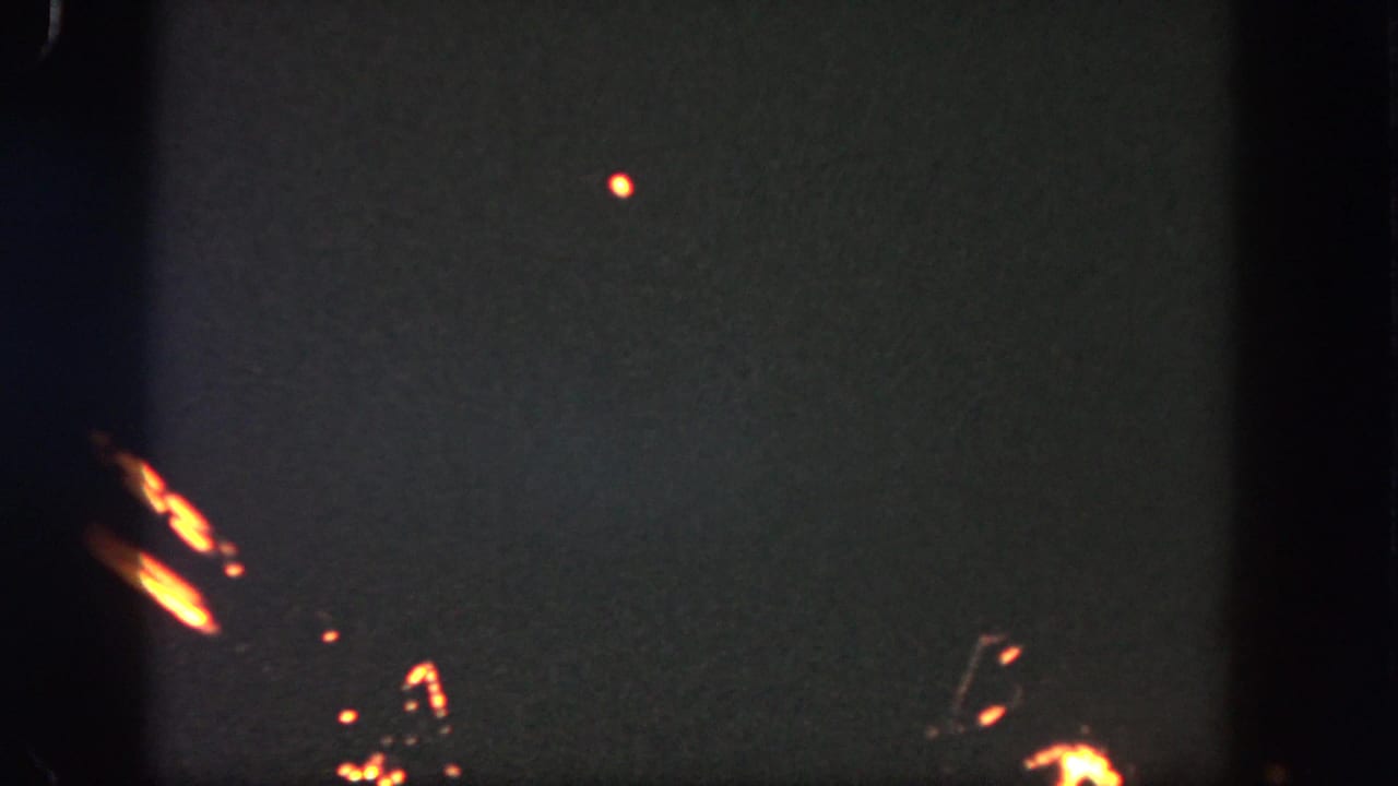 Dark night sky with small orange fireworks trails and film edge shadows.