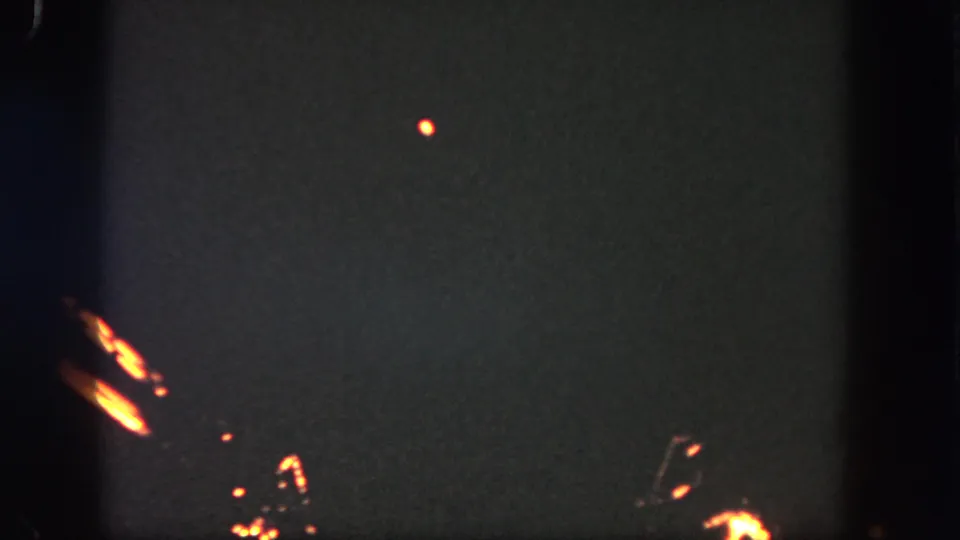 1962 Disneyland home-movie frame showing orange fireworks traces against a dark night sky with visible 8mm grain and edge shadows.