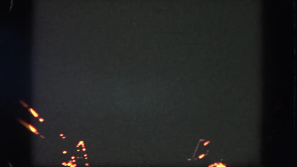 1962 Disneyland 8mm frame showing dim orange fireworks traces near the bottom edge of a dark night sky.