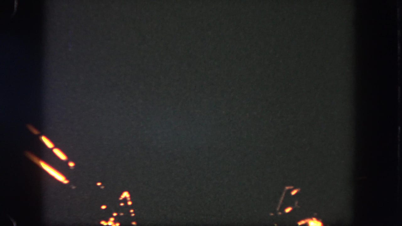A visitor-shot 8mm frame from Disneyland shows orange firework trails and scattered sparks against a dark night sky.