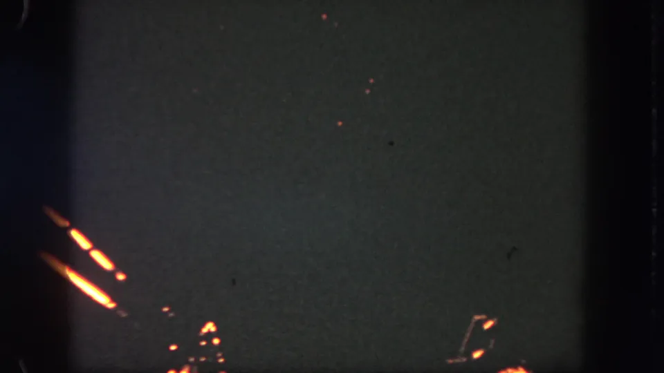 The 8mm frame shows low, orange fireworks and faint sparks in a dark sky during the Disneyland nighttime display.