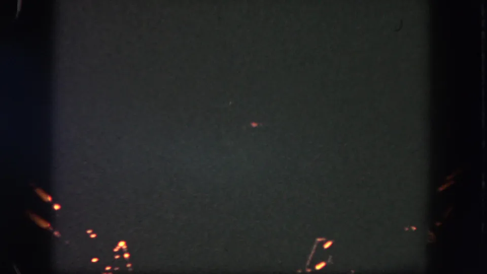 1962 Disneyland home-movie frame showing a dark night sky with small orange fireworks sparks and low-light film texture.