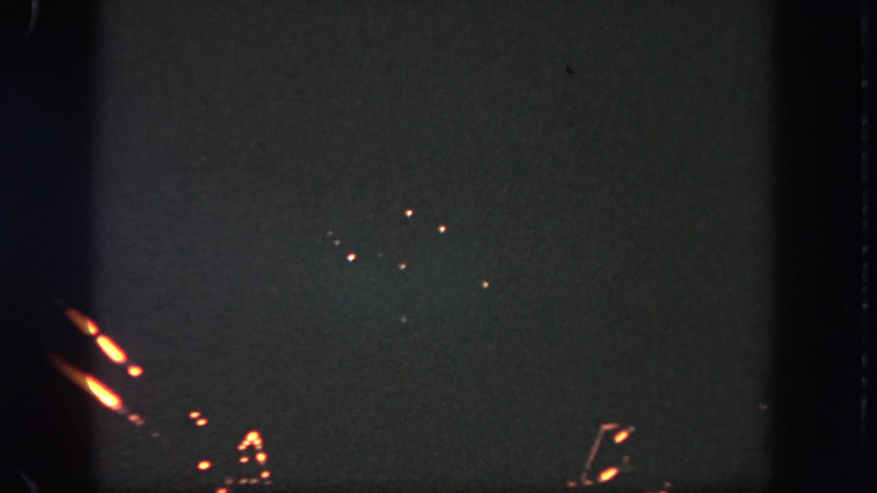 Visitor-shot 1962 Disneyland fireworks frame with scattered orange sparks, short light streaks, and visible low-light grain.