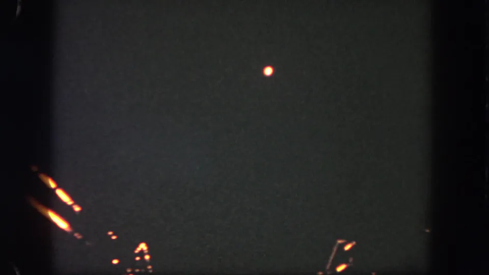 1962 Disneyland fireworks footage showing one bright point in the night sky with faint edge flares and 8mm grain.