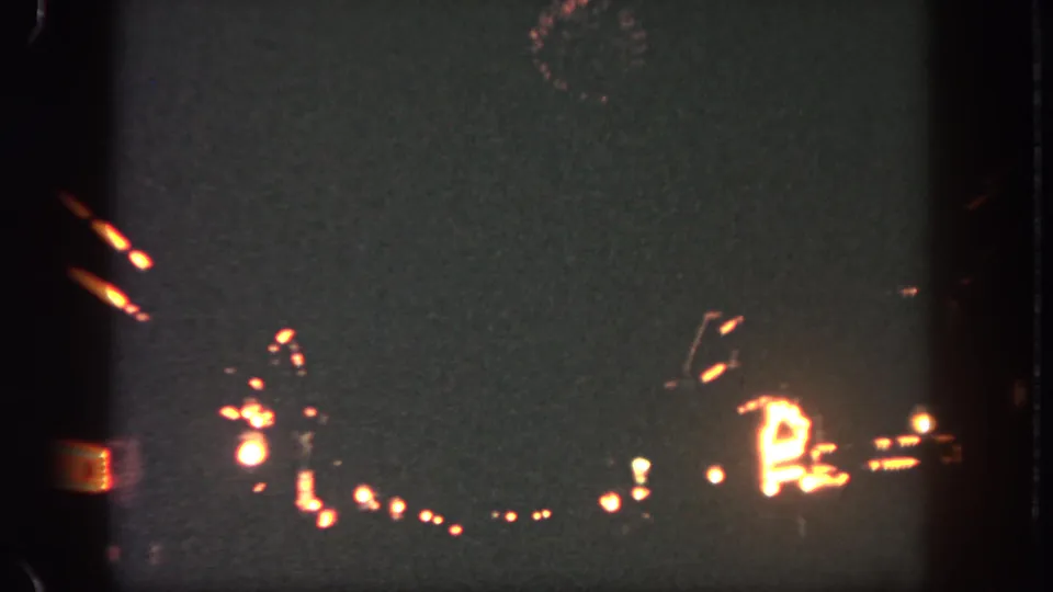 1962 Disneyland night view from 8mm footage, showing warm Main Street lights and small fireworks against a dark sky.