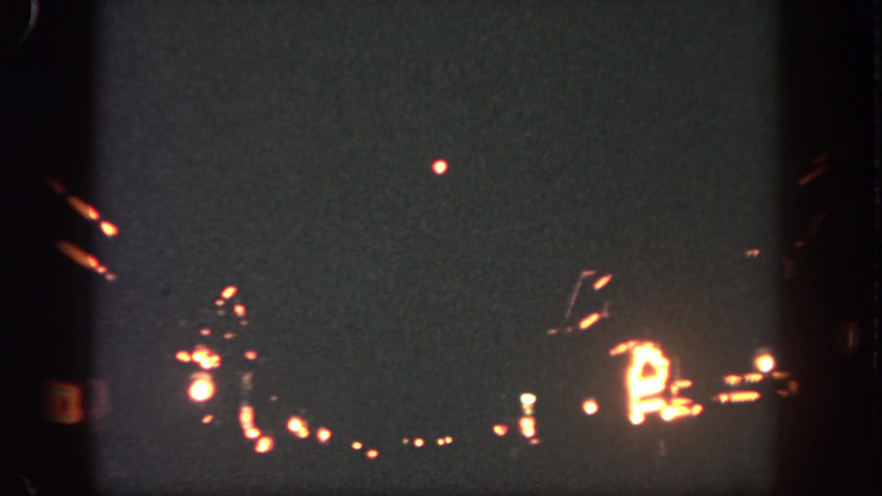 8mm Disneyland night frame with a bright firework point above blurred rows of warm park lighting.