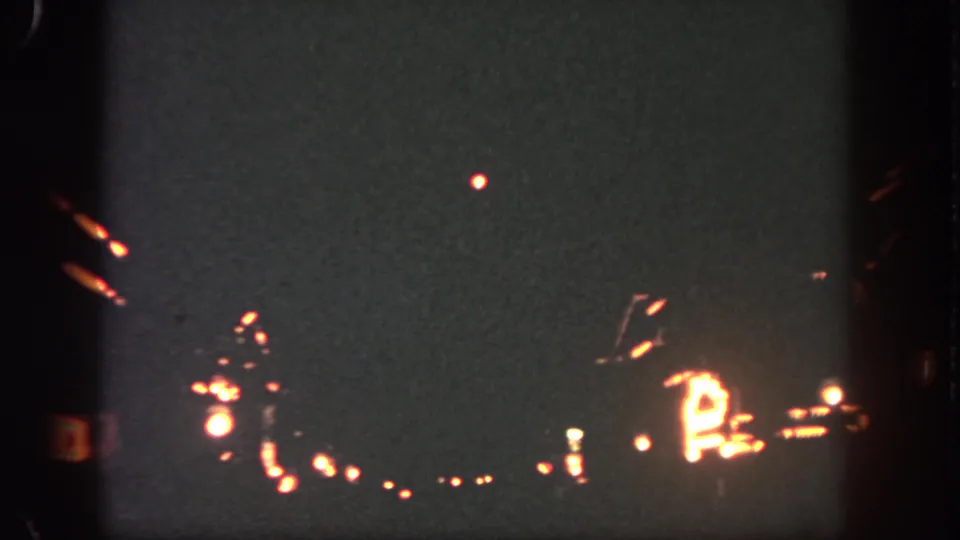 8mm Disneyland night frame with a bright firework point above blurred rows of warm park lighting.