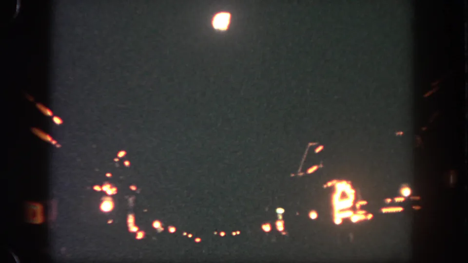 8mm Disneyland night frame showing a bright firework glow above warm, blurred park lighting and visible film grain.