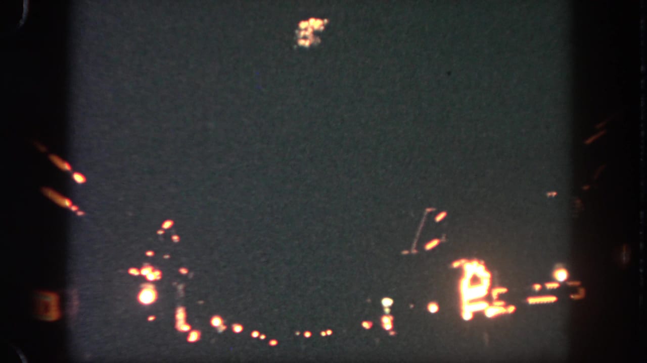 1962 Disneyland home-movie frame showing dark nighttime sky, distant park lights, and a small orange-white pyrotechnic burst.