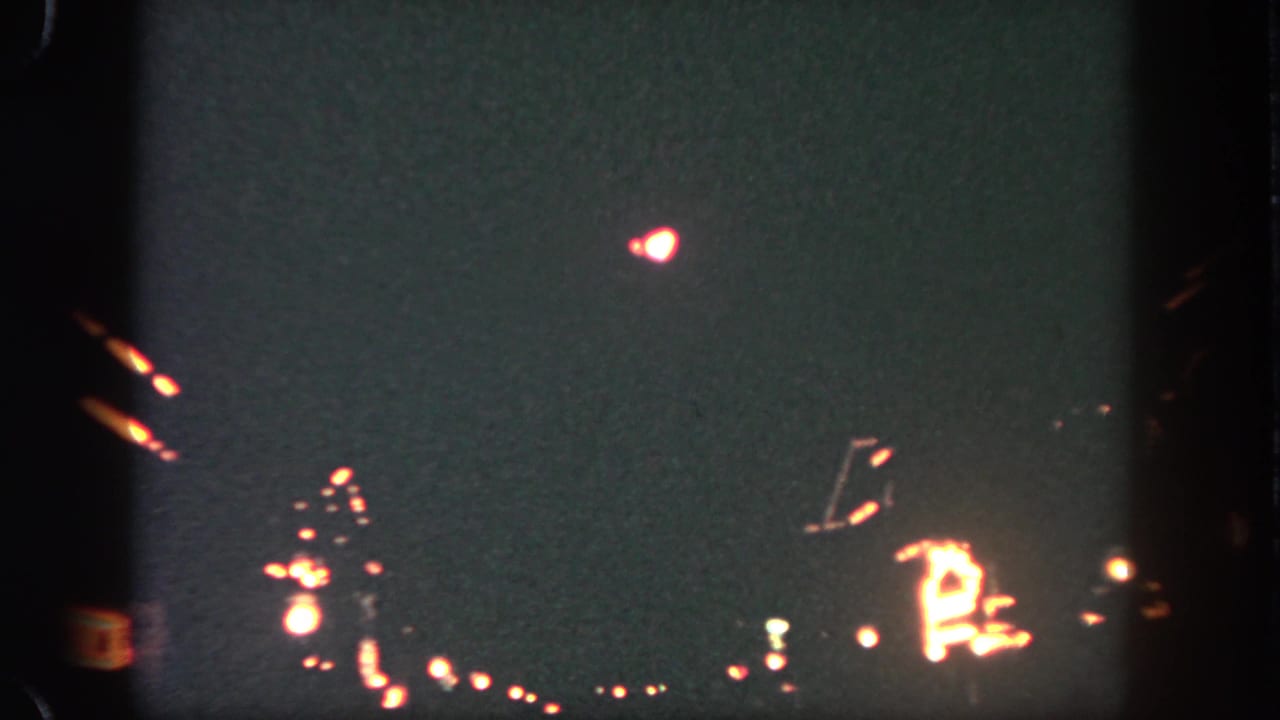 Dark sky with a bright red-white burst above distant illuminated shapes.