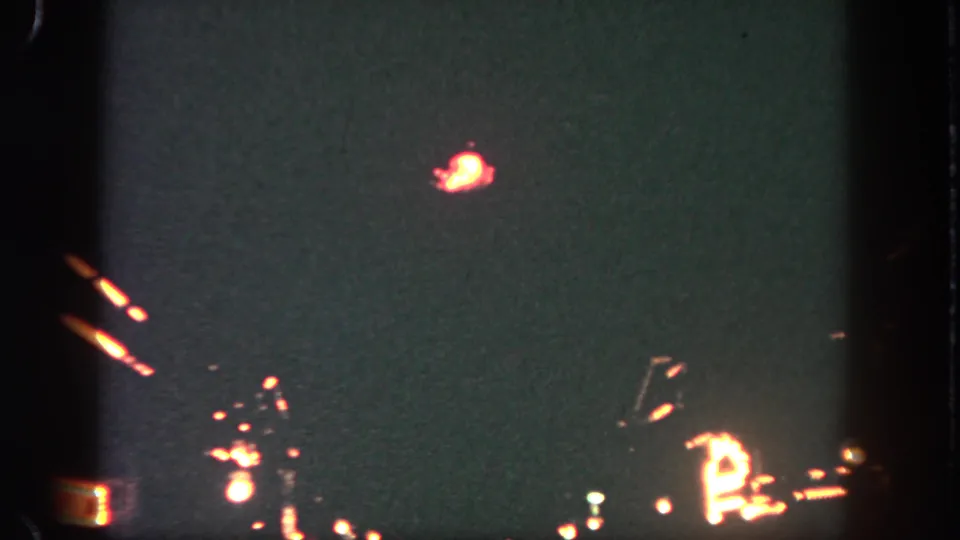 1962 Disneyland nighttime frame with a bright orange pyrotechnic burst over small distant lights and visible 8mm film edges.