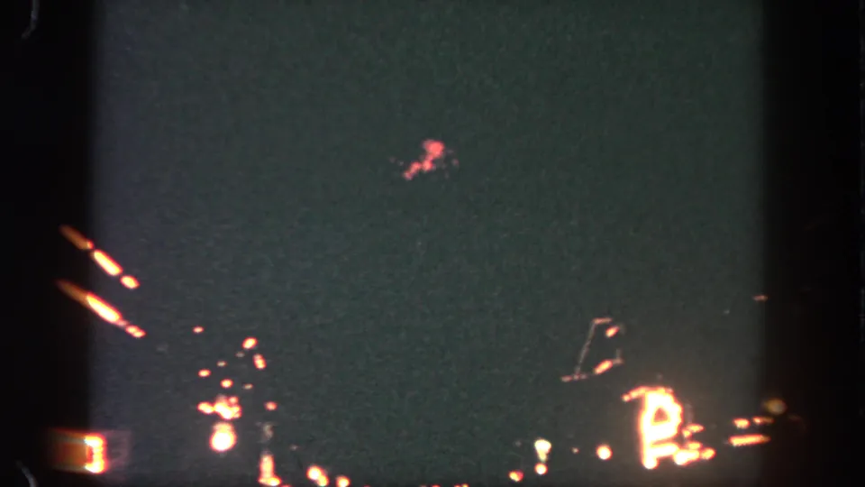 1962 Disneyland home-movie frame showing small red and white fireworks glowing in a dark night sky.