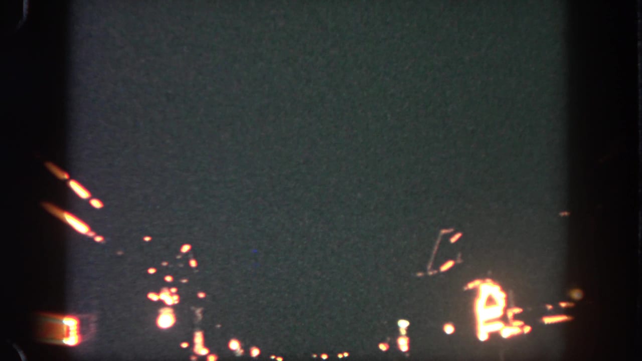 Nighttime 8mm frame from the Disneyland fireworks clip with faint arcs and glowing points near the lower edge.