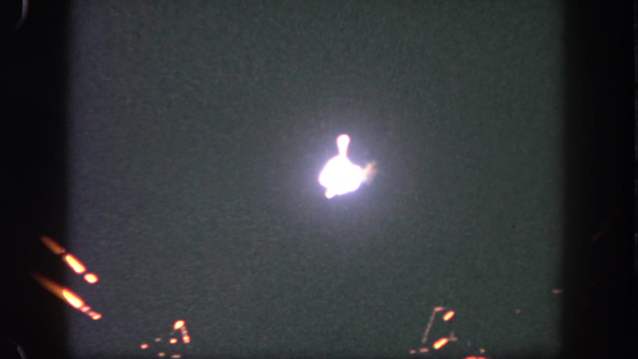 Bright firework bloom in a dark, grainy sky with small light streaks near the frame edge.