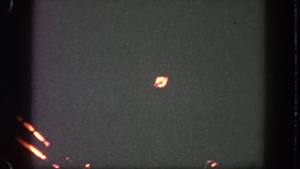 1962 Disneyland nighttime home-movie frame with a faint glowing ember in a dark, grain-textured sky.