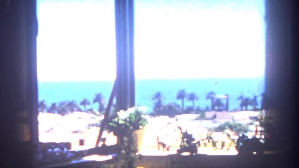 Daytime vacation view from a window toward palms, rooftops, and ocean, following the 1962 California home-movie sequence.