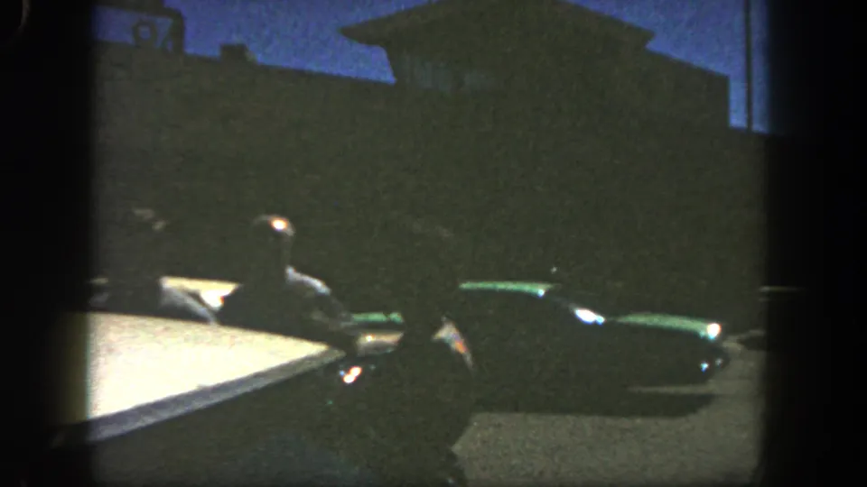 1962 San Diego frame showing silhouetted pedestrians and parked cars against a dark building and blue evening sky.
