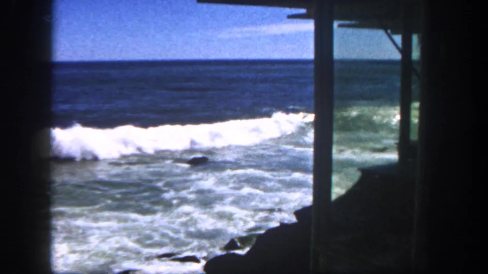 Daytime San Diego coastal frame showing waves breaking over rocks, partly framed by a wooden structure.