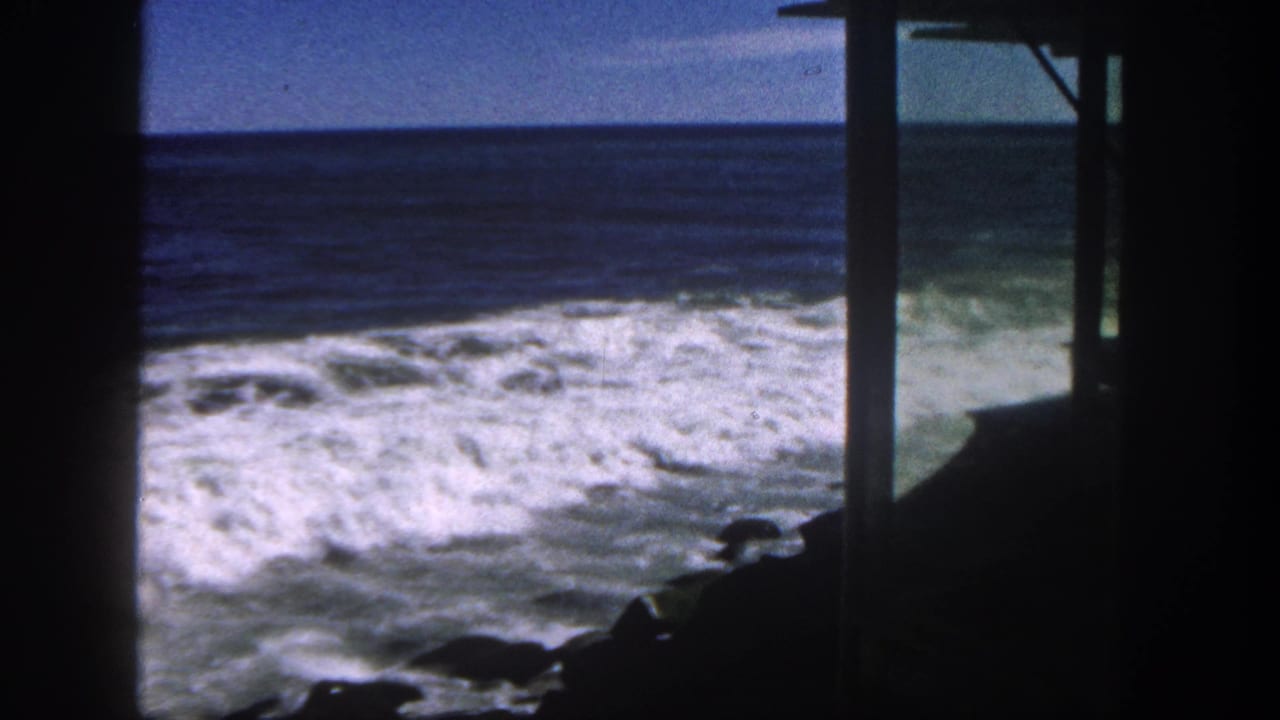 A 1962 San Diego ocean view shows churning Pacific surf framed by dark posts and a roofline shadow.