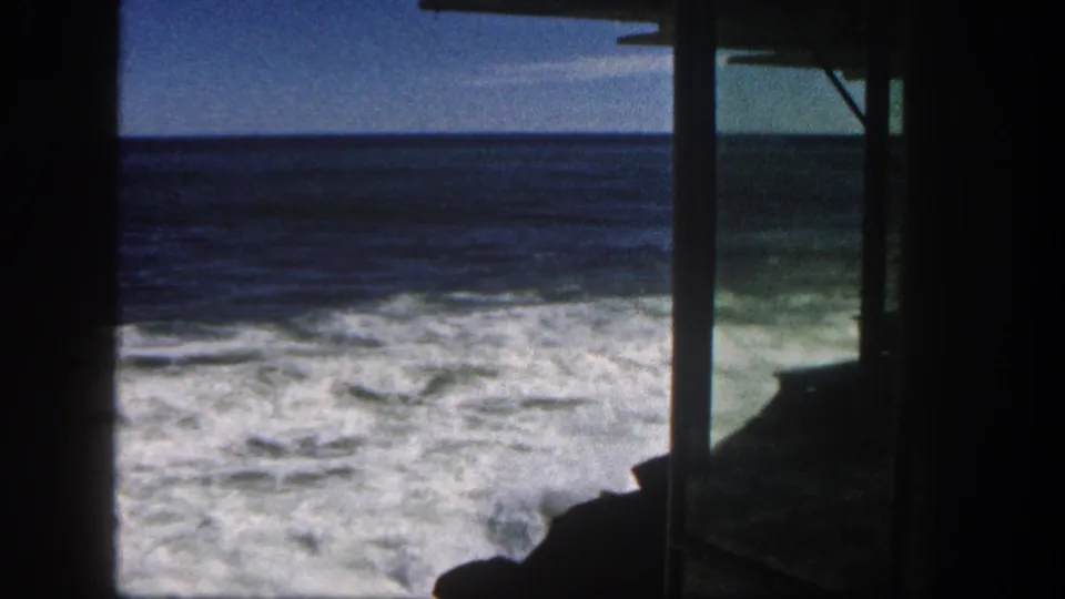 Foamy Pacific waves and a blue horizon are filmed from a shaded seaside structure in San Diego in 1962.