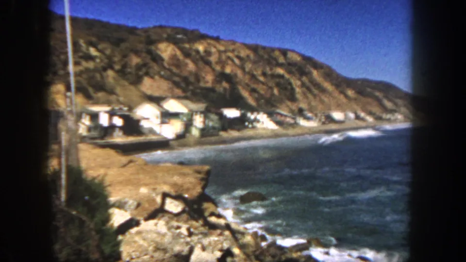 1962 San Diego coastal view showing small beach houses, a rocky hillside, shoreline, and blue ocean.