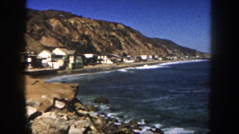 Vintage 8mm San Diego shoreline frame with hillside, beach houses, blue ocean, and surf along the coast.