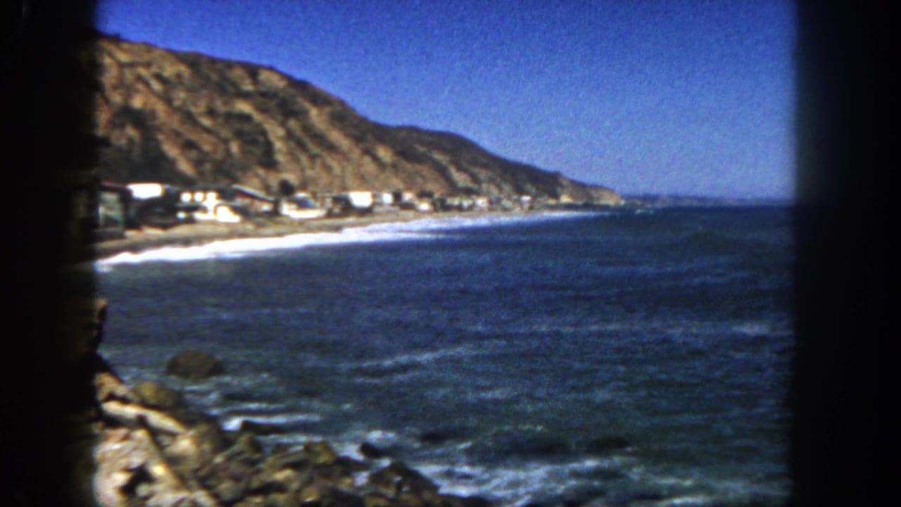 San Diego shoreline in 1962, showing ocean surf, beach houses, rocky slope, and a dark 8mm film border.
