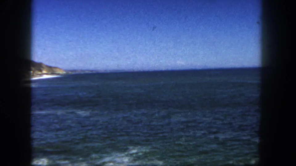 1962 San Diego home-movie frame showing dark blue ocean, a level horizon, faint surf, and a small cliff edge at the left side.