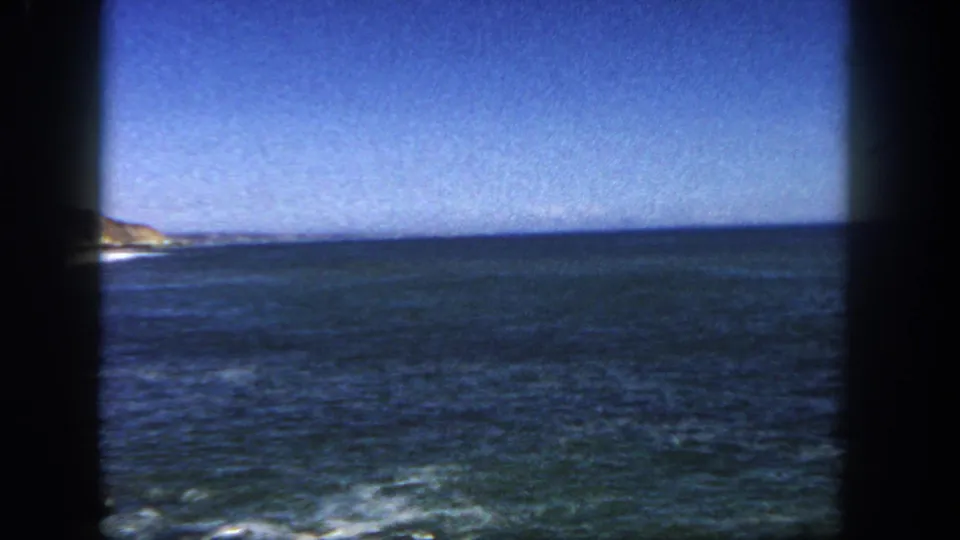 1962 San Diego coastal view with open water, blue sky, a distant shoreline at left, and dark 8mm frame borders.