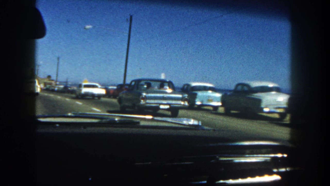 1962 San Diego in-car view of classic automobiles lining a coastal highway with ocean visible past the road.